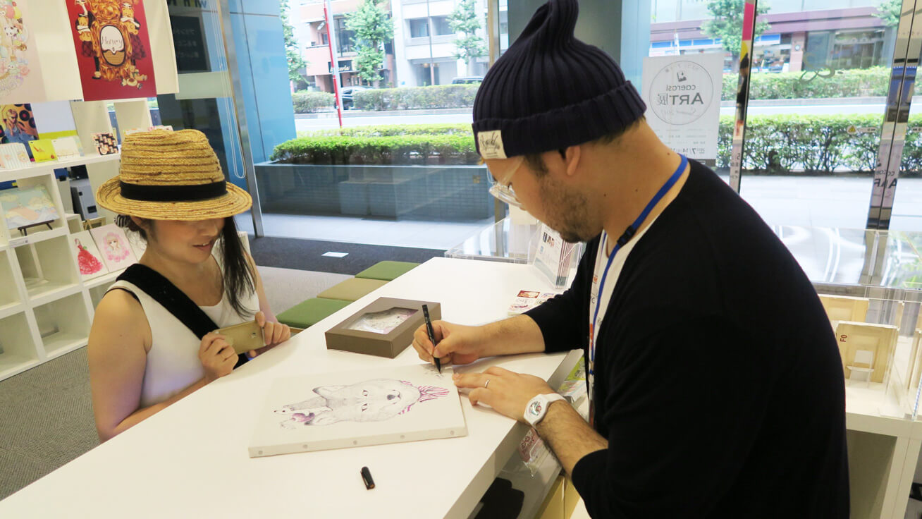 Yushi Iwasaki signing artwork made with a UV printer before handing it to a customer.