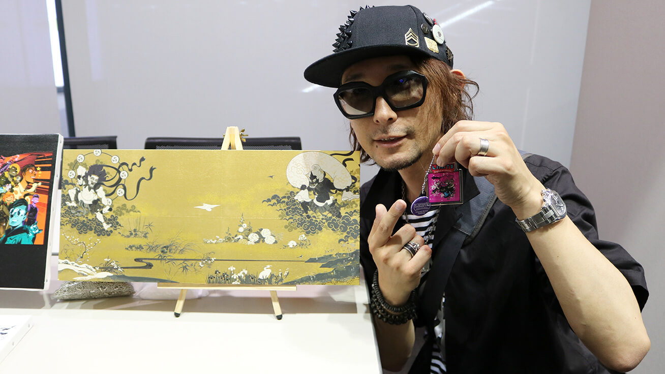 Baron Ueda (Japan) holding a one-of-a-kind creation he designed and standing in front of artwork he produced using a Roland DG UV printer.